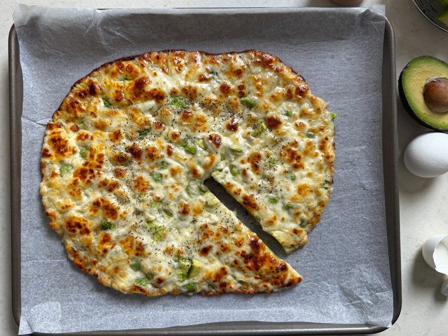 Golden, crisp 3-ingredient avocado bread on a parchment-lined baking tray, one wedge cut out.