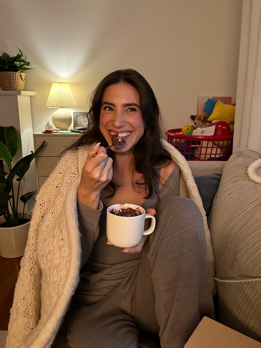 A woman enjoying a chocolate mug cake on the sofa